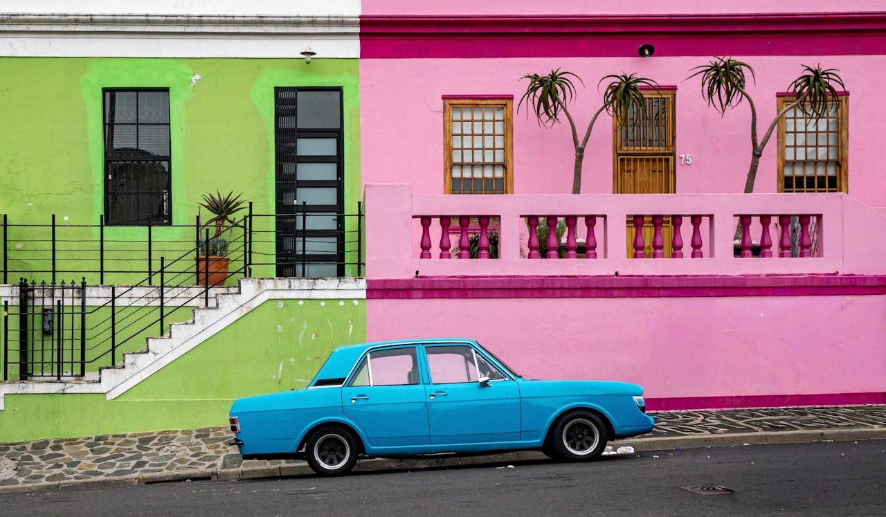 our-services-3 Vibrant pink and green houses with a classic blue car in Bo-Kaap, Cape Town.